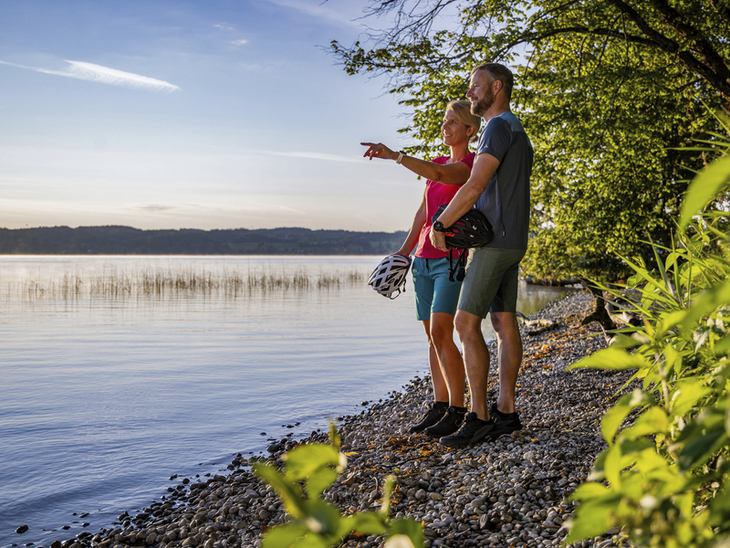 Paar macht Radtour-Pause am Starnberger See auf Kiesstrand bei schönem Wetter.
