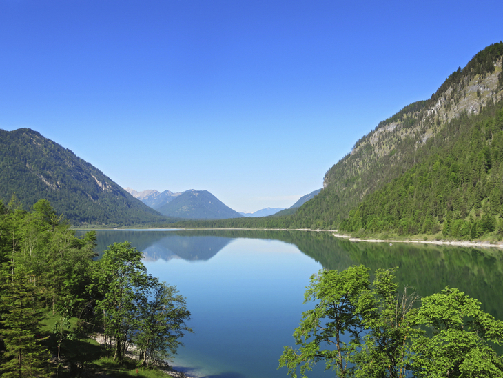 Blick auf den Sylvensteinspeicher umgeben von Bergen unter klarem blauem Himmel.