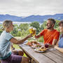 Drei Personen stoßen bei Brotzeit mit Bier am Tegernsee an.