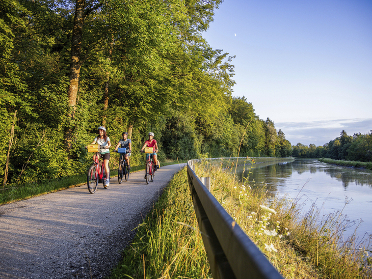 Radfahrer auf einem Weg entlang der Isar mit Bäumen und Wasser im Hintergrund.