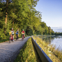 Radfahrer auf einem Weg entlang der Isar mit Bäumen und Wasser im Hintergrund.
