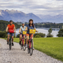 Radfahrer auf Schotterweg mit Blick auf See und Alpen im Hintergrund