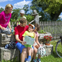Familie macht Radpause, Vater hält Karte, Kinder schauen zu, Sommerlandschaft im Hintergrund.