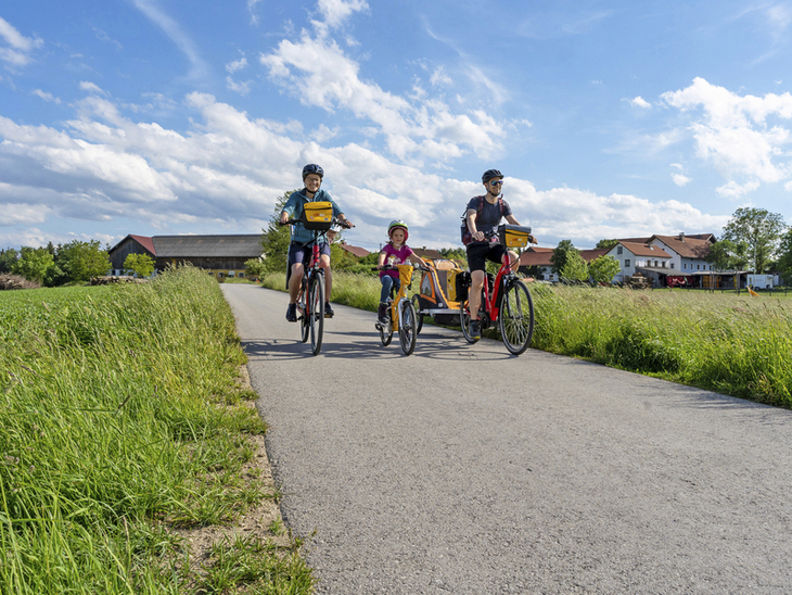 Familie auf Fahrradtour auf einer ländlichen Straße bei Sonnenschein.