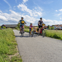 Familie auf Fahrradtour auf einer ländlichen Straße bei Sonnenschein.
