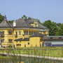 Gelbes Schloss Hellbrunn in Salzburg mit modernem Anbau und Garten im Vordergrund.