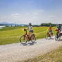 Drei Radfahrer auf einem Schotterweg im Salzburger Seenland bei sonnigem Wetter.
