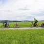 Familie mit Fahrrädern auf einem Radweg in grüner Landschaft.