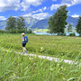 Person wandert auf einem Pfad am See im Salzkammergut, umgeben von Wiesen und Bergen.