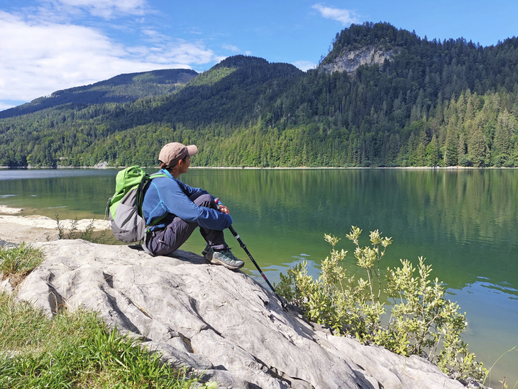 Wanderer sitzt auf einem Felsen am Schwarzensee und schaut über das Wasser.