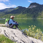 Wanderer sitzt auf einem Felsen am Schwarzensee und schaut über das Wasser.