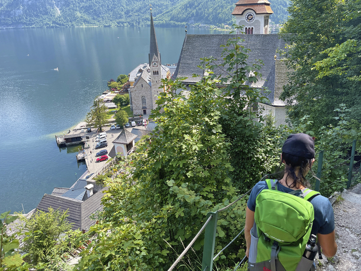 Person wandert auf einem Pfad hinab nach Hallstatt mit Blick auf den See und Kirche.