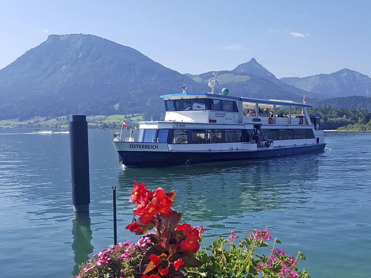 Ein Schiff auf dem Wolfgangsee mit Bergen im Hintergrund und Blumen im Vordergrund.