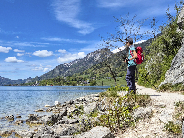 Wanderin mit Rucksack am Wolfgangseeufer in malerischer Berglandschaft.