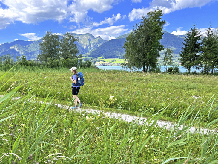 Wanderer spaziert am Seeuferweg im Salzkammergut mit Bergen im Hintergrund.