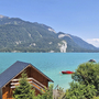 Holzhütte am Wolfgangsee mit Bergen im Hintergrund und blauem Himmel.