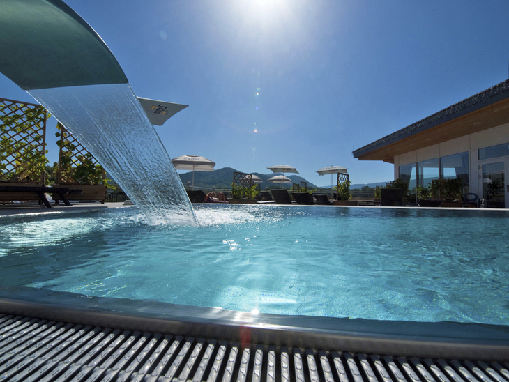 Pool des Gartenhotel Pfeffel Dürnstein bei sonnigem Wetter, mit Wasserfall und Liegestühlen.