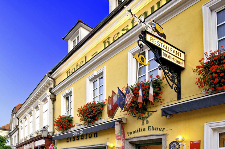 Gelbes Hotel mit Restaurant, Schildern und blühenden Blumenkästen außen.