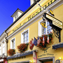 Gelbes Hotel mit Restaurant, Schildern und blühenden Blumenkästen außen.