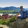 Wanderin betrachtet Donaublick von Ruine Dürnstein, umgeben von Hügeln und Flusslandschaft.