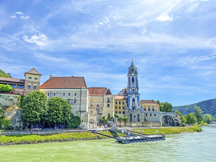 Stift Dürnstein mit blauem Kirchturm am Donauufer bei sonnigem Wetter.