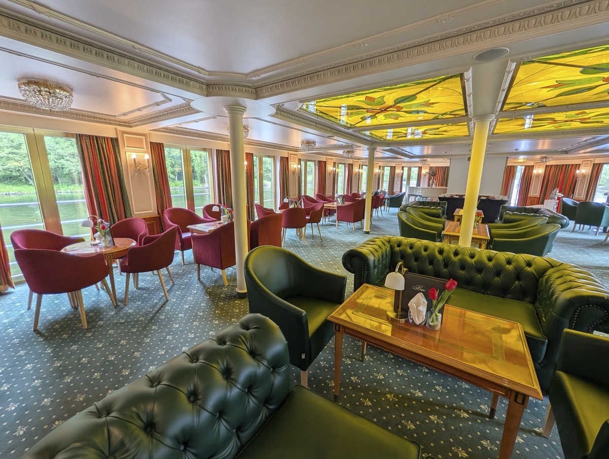 Lounge mit grünen Sofas und roten Sesseln auf einem Schiff.