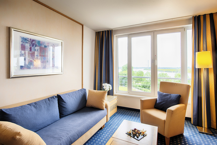 Wohnbereich einer Hotelsuite mit Sofa, Sessel und Fenster mit Blick nach draußen.