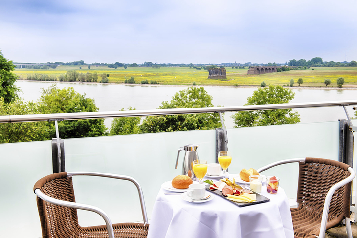 Tisch mit Frühstück auf Balkon mit Flussblick im Hotel in Wesel.
