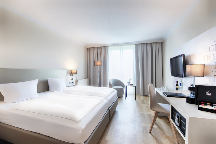Modernes Hotelzimmer mit zwei Betten, Schreibtisch, TV und Fenster.
