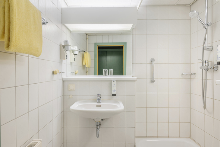 Badezimmer im Hotel mit Waschbecken, Dusche, Handtüchern und Spiegel.
