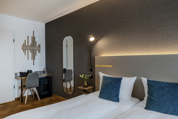 Hotelzimmer mit Doppelbett, Schreibtisch, Spiegel und dekorativer Wandkunst.