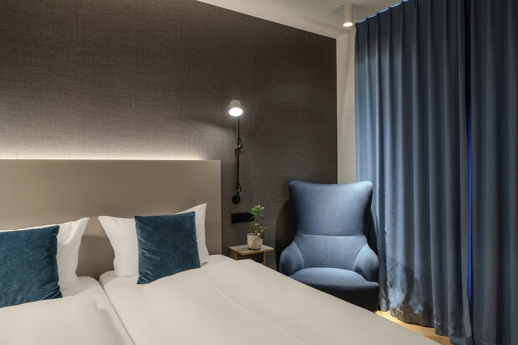 Modernes Hotelzimmer mit Bett, Sessel und Vorhängen.