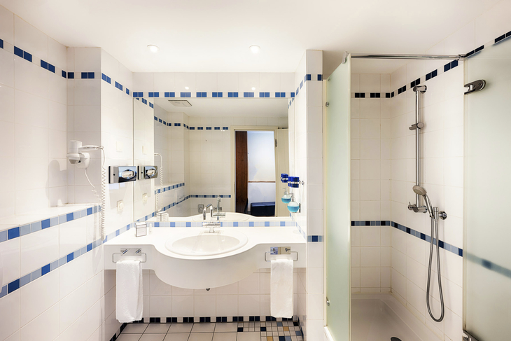 Modernes Hotelbadezimmer mit Dusche und großem Spiegel.