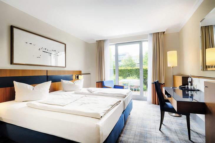 Doppelzimmer mit großen Fenstern und Schreibtisch, helle und moderne Einrichtung.
