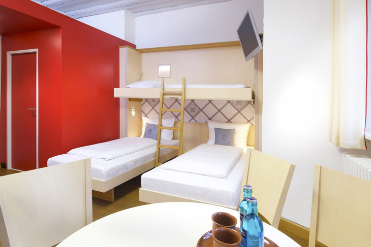 Zwei Einzelbetten und ein Hochbett in einem Hotelzimmer mit hellem Holzinterieur.