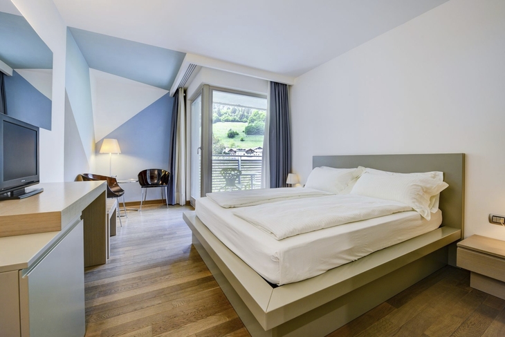 Hotelzimmer mit Doppelbett, Holzboden und Bergblick durch ein Fenster.