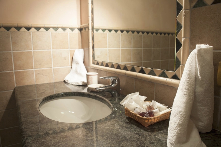 Badezimmer mit Waschbecken und Spiegel, Handtuch und Seifenkorb auf dem Tresen.
