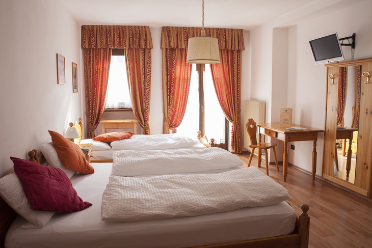 Helles Zimmer mit zwei Betten, roten Vorhängen und Schreibtisch.