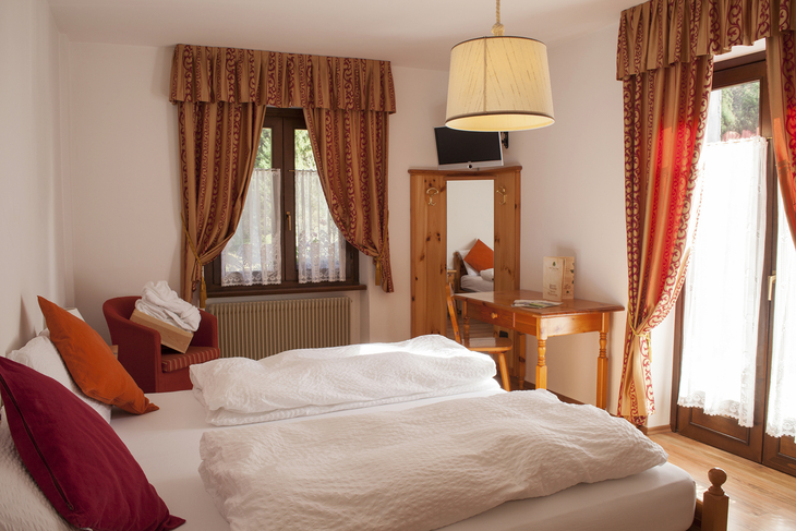 Helles Schlafzimmer mit Doppelbett, zwei Fenstern, Tisch und TV.