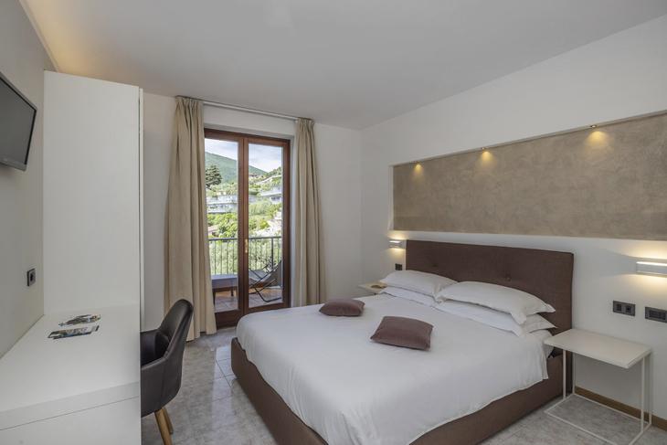 Hotelzimmer mit Doppelbett, Schreibtisch und Balkon mit Blick auf die Berge.