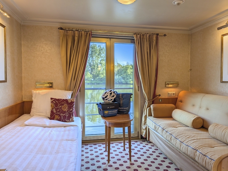 Kabine auf einem Flusskreuzfahrtschiff mit Bett, Sofa und Blick auf den Fluss.