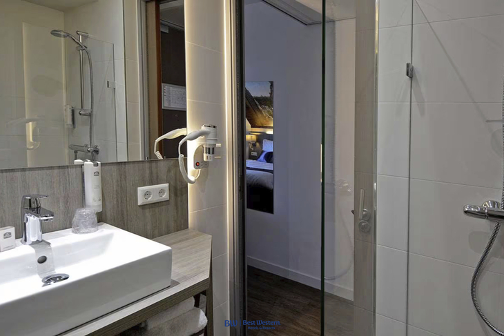 Badezimmer mit Waschbecken, Spiegel und Dusche in einem Hotelzimmer.