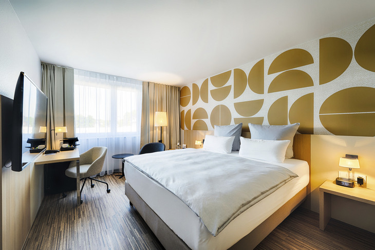 Modernes Hotelzimmer mit Doppelbett und Schreibtisch, helle Wanddekoration.