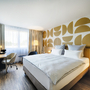 Modernes Hotelzimmer mit Doppelbett und Schreibtisch, helle Wanddekoration.