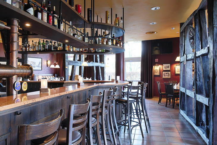 Gemütliche Hotelbar mit Holzdekor und hohen Barhockern im Welcome Hotel Paderborn.
