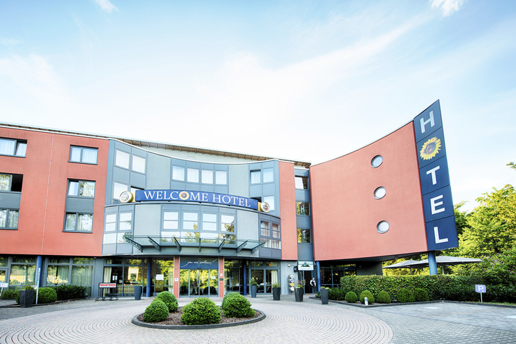 Eingang des Welcome Hotels in Paderborn mit auffälliger Fassade und Schildern.