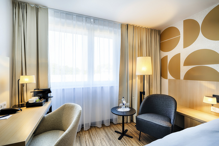 Modernes Hotelzimmer mit Schreibtisch, Sesseln und großem Fenster.