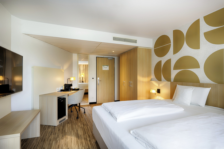 Modernes Hotelzimmer mit Doppelbett, Schreibtisch und Wanddekoration.