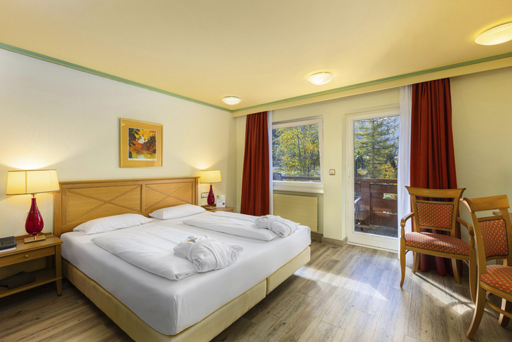 Doppelzimmer mit Doppelbett, zwei Stühlen, Fenster und Wandbild.