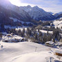 Verschneite Alpenlandschaft mit Hütten und Bergen im Hintergrund.